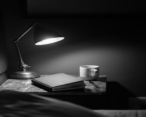 A warm desk lamp illuminating a book page on a nightstand for a relaxed night routine